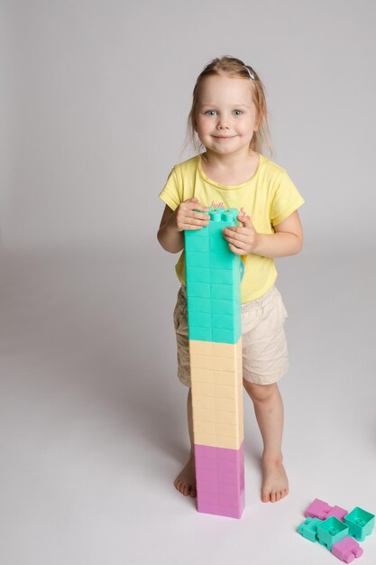 Retrato de una niña encantadora sosteniendo bloques de colores altos construidos por ella misma Linda niña sonriente jugando con bloques de plástico de colores en el estudio Ella está sonriendo felizmente a la cámara