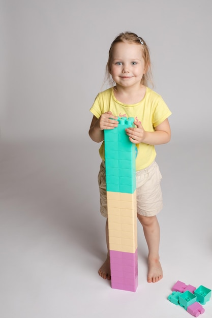 Foto gratuita retrato de una niña encantadora sosteniendo bloques de colores altos construidos por ella misma linda niña sonriente jugando con bloques de plástico de colores en el estudio ella está sonriendo felizmente a la cámara