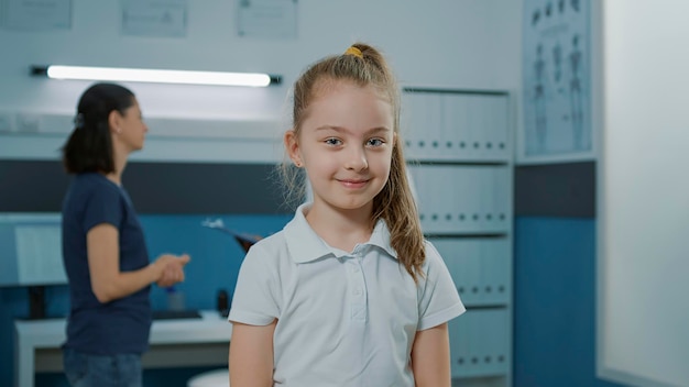 Retrato de una niña esperando para hacer un examen médico con un médico, sentada en la cama en el gabinete. Niño en el consultorio preparándose para hablar con el pediatra en la cita de visita de control. Cuidado de la salud