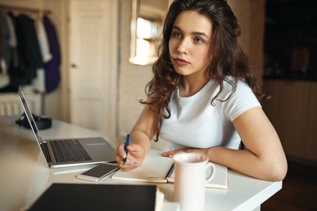 Retrato de niña estudiante pensativa pensativa que estudia desde casa, sentada en su lugar de trabajo frente a la computadora portátil abierta