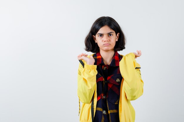 Retrato de niña extendiendo las palmas en camisa a cuadros, chaqueta y mirando melancólica vista frontal