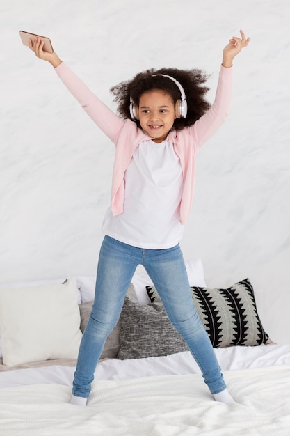 Retrato de niña feliz bailando música en la cama