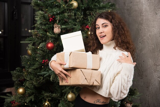 Retrato de niña feliz con cabello rizado sosteniendo una pila de regalos en un envoltorio