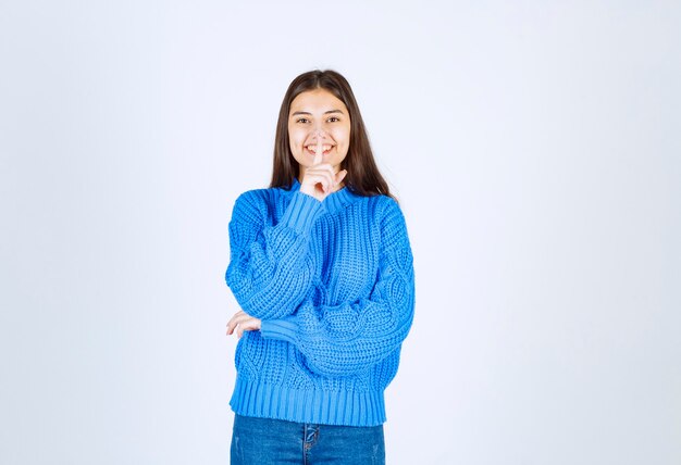 Retrato de niña feliz en suéter azul dando señal de silencio en blanco.