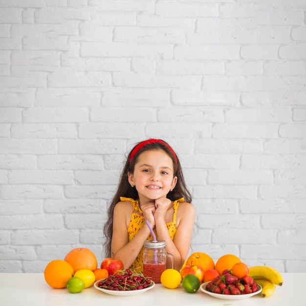 Retrato de niña con frutas sobre el escritorio blanco