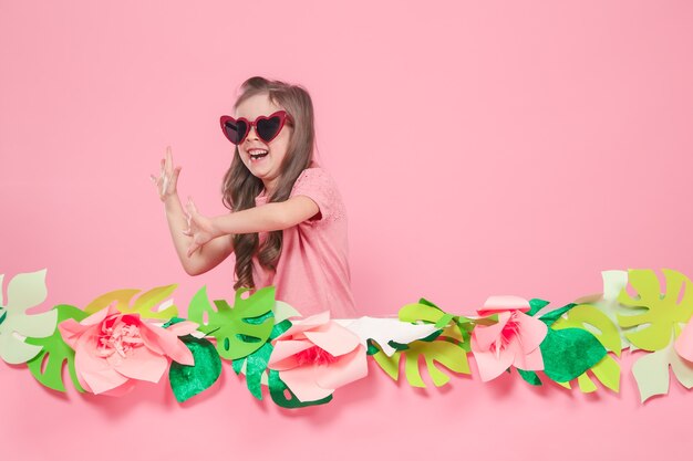 Retrato de una niña con gafas de sol en una pared rosa