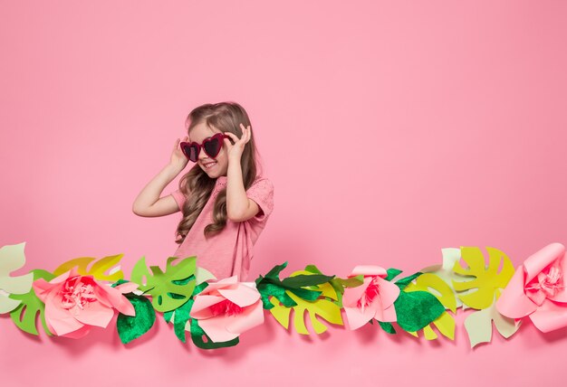 Retrato de una niña con gafas de sol sobre un fondo rosa