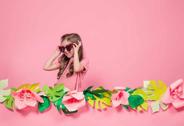 Retrato de una niña con gafas de sol sobre un fondo rosa