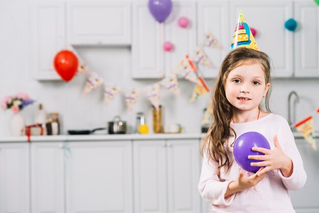 Retrato de una niña con globo morado de pie en la cocina