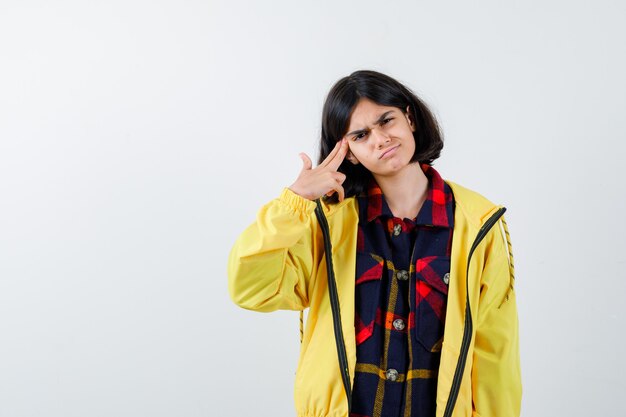 Retrato de niña haciendo gesto de suicidio en camisa a cuadros, chaqueta y mirando estresado vista frontal