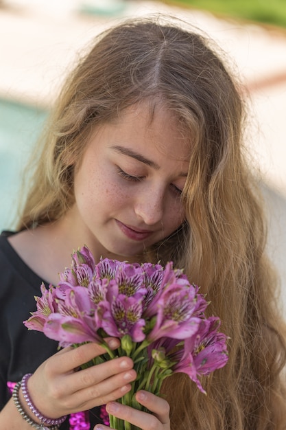 Retrato de niña hermosa que huele a flores afuera en camiseta negra durante el día.