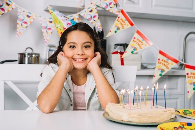 Foto gratuita retrato de niña hermosa sonriente con pastel de cumpleaños en la mesa