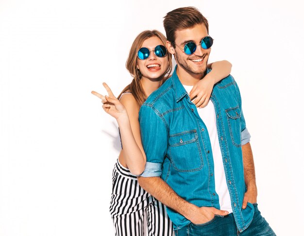 Retrato de niña hermosa sonriente y su novio guapo riendo. Feliz pareja alegre en gafas de sol. y mostrando el signo de la paz