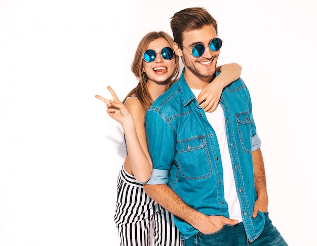 Retrato de niña hermosa sonriente y su novio guapo riendo. Feliz pareja alegre en gafas de sol. y mostrando el signo de la paz