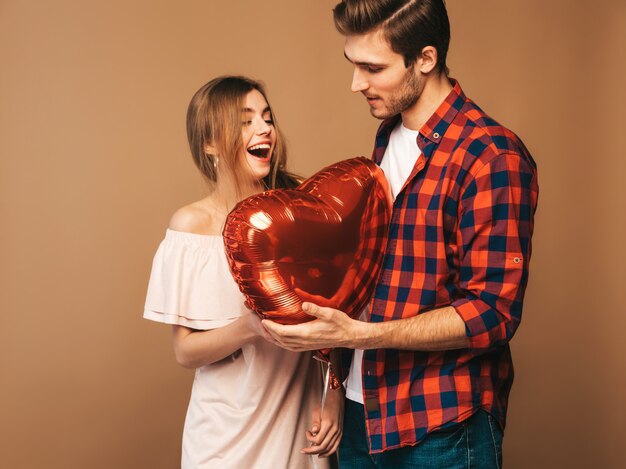 Retrato de niña hermosa sonriente y su novio guapo sosteniendo globos en forma de corazón y riendo. Feliz pareja de enamorados. Feliz día de San Valentín