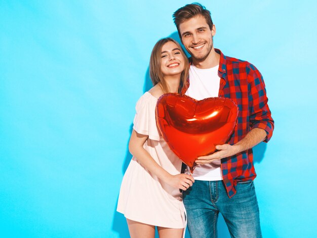 Retrato de niña hermosa sonriente y su novio guapo sosteniendo globos en forma de corazón y riendo. Feliz pareja de enamorados. Feliz día de San Valentín