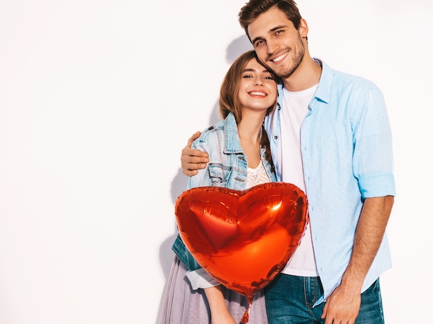 Retrato de niña hermosa sonriente y su novio guapo sosteniendo globos en forma de corazón y riendo. Feliz pareja de enamorados. Feliz día de San Valentín