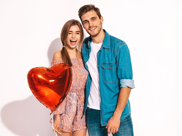 Retrato de niña hermosa sonriente y su novio guapo sosteniendo globos en forma de corazón y riendo. Feliz pareja de enamorados. Feliz día de San Valentín