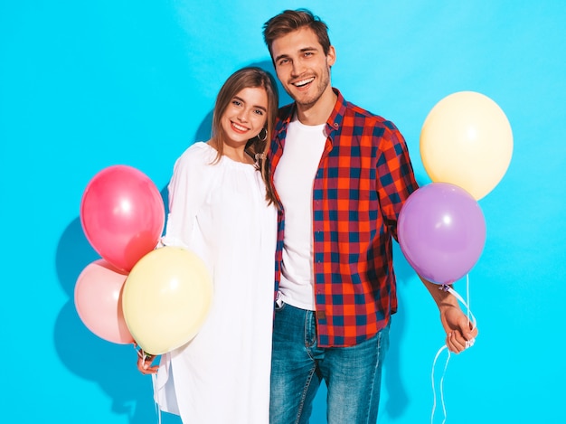 Retrato de niña hermosa sonriente y su novio guapo sosteniendo un montón de globos de colores y riendo. Feliz cumpleaños