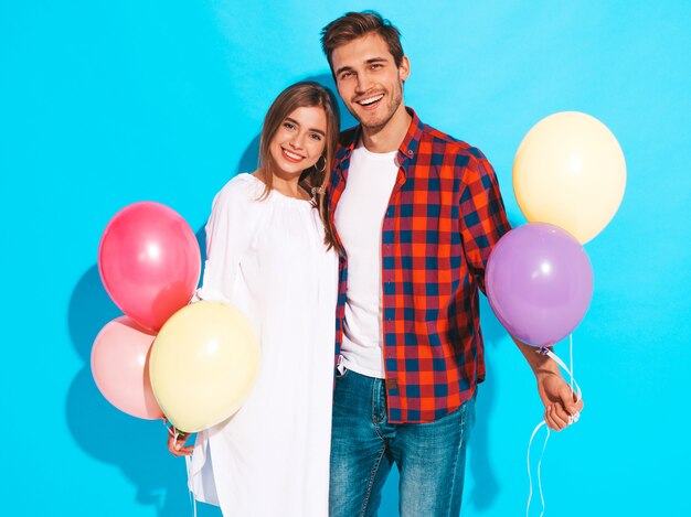 Retrato de niña hermosa sonriente y su novio guapo sosteniendo un montón de globos de colores y riendo. Feliz cumpleaños