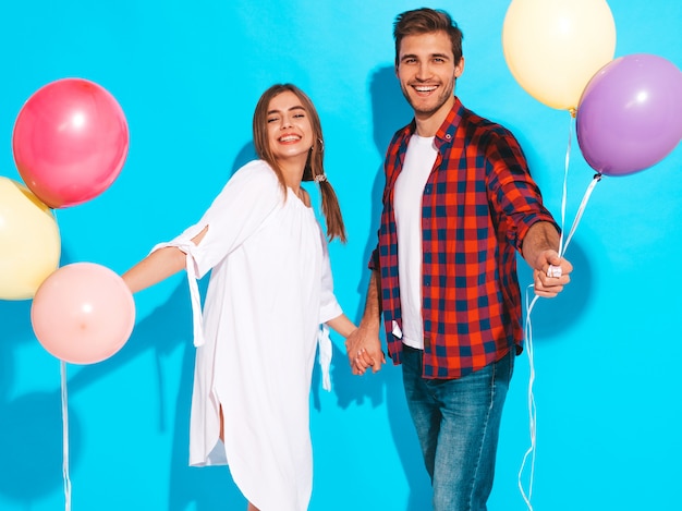 Retrato de niña hermosa sonriente y su novio guapo sosteniendo un montón de globos de colores y riendo. Feliz cumpleaños