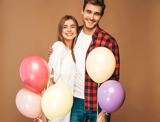 Retrato de niña hermosa sonriente y su novio guapo sosteniendo un montón de globos de colores y riendo. Feliz pareja de enamorados. Feliz cumpleaños