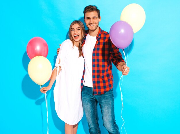 Retrato de niña hermosa sonriente y su novio guapo sosteniendo un montón de globos de colores y riendo. Feliz pareja de enamorados. Feliz cumpleaños