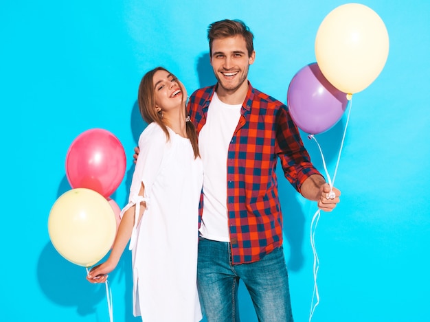 Retrato de niña hermosa sonriente y su novio guapo sosteniendo un montón de globos de colores y riendo. Pareja feliz. Feliz cumpleaños