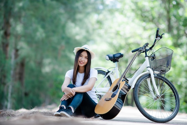 Retrato de niña hermosa tocando la guitarra con bicicleta en la naturaleza