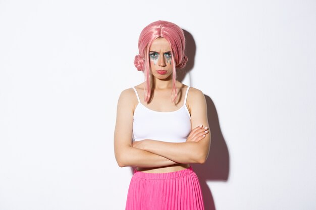 Retrato de niña linda enojada con peluca rosa y maquillaje glamour, brazos cruzados en el pecho y enfurruñado enojado