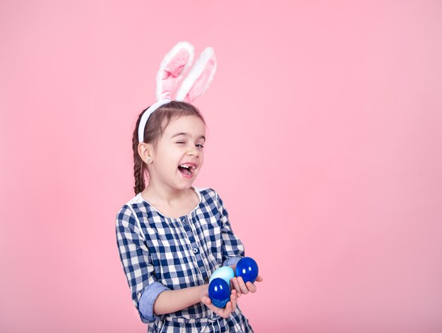 Retrato de una niña linda con los huevos de Pascua en un fondo rosado.