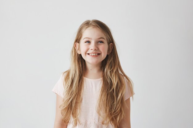 Retrato de niña linda con largo cabello claro sonriendo mirando al revés en coloridos globos voladores con expresión feliz y emocionada.