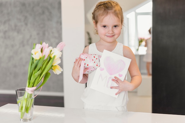 Retrato de niña linda de pie con caja de regalo y tarjeta de felicitación