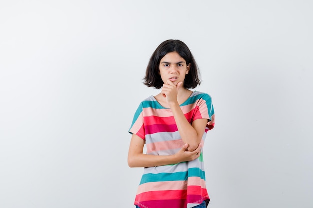 Retrato de niña manteniendo la mano en la barbilla en camiseta y mirando molesto vista frontal