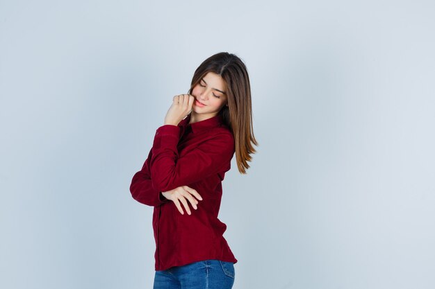 Retrato de niña manteniendo la mano cerca de la boca, mirando hacia abajo en camisa casual y luciendo soñadora