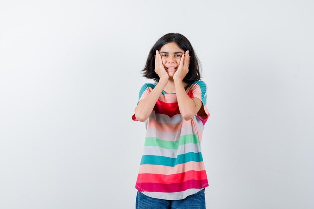 Retrato de niña manteniendo las manos en las mejillas en camiseta y mirando alegre vista frontal