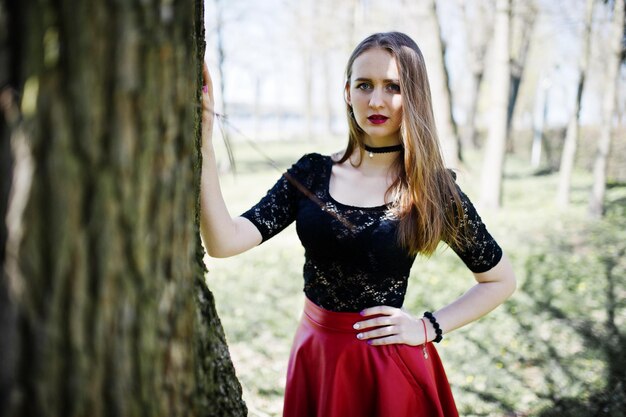 Retrato de niña con maquillaje brillante con labios rojos collar de gargantilla negra en el cuello y falda de cuero rojo en Spring Park