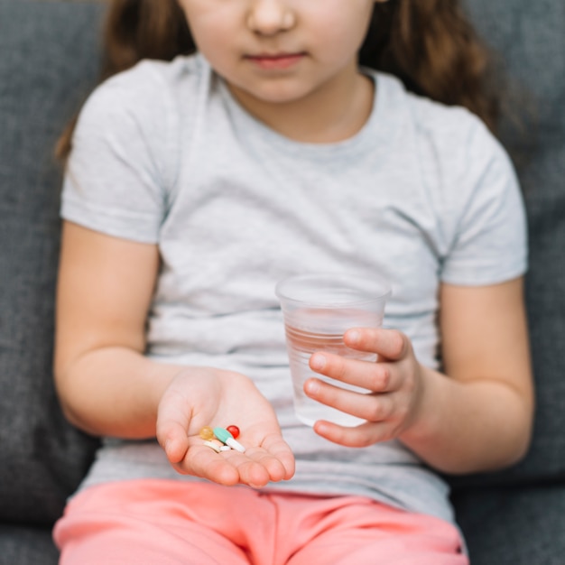 Retrato de una niña con medicina y vaso de agua en la mano