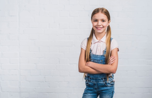 Foto gratuita retrato de una niña mirando a la cámara de pie contra la pared de ladrillo blanco