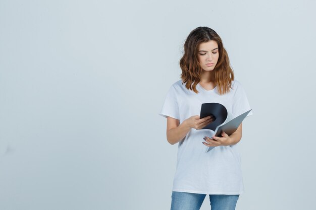 Retrato de niña mirando por encima de las notas en la carpeta en la camiseta blanca y mirando la vista frontal enfocada