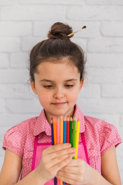 Retrato de una niña mirando lápices multicolores en la mano