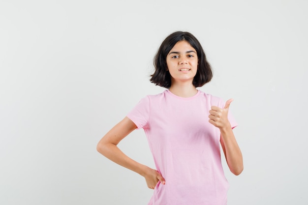 Retrato de niña mostrando el pulgar hacia arriba en camiseta rosa y mirando alegre vista frontal