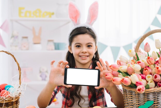 Retrato de una niña con orejas de conejo mostrando su teléfono inteligente en el día de Pascua