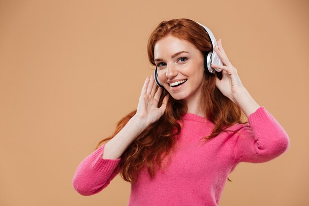 Retrato de una niña pelirroja amigable feliz escuchando música con auriculares