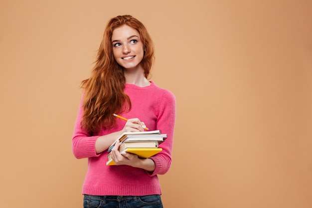 Foto gratuita retrato de una niña pelirroja pensativa feliz sosteniendo libros