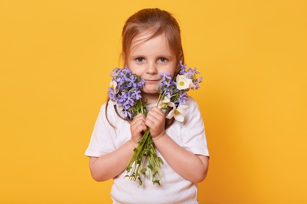 Retrato de niña pequeña con ramo de flores de jardín aislado sobre amarillo