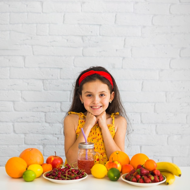 Foto gratuita retrato de una niña de pie detrás de la mesa con frutas orgánicas frescas