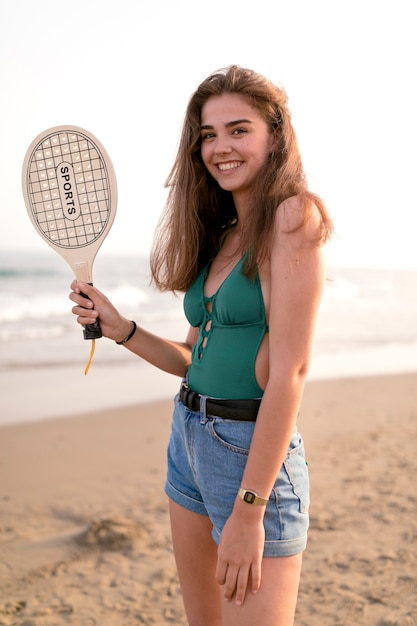 Retrato de una niña de pie en la playa con raqueta de tenis