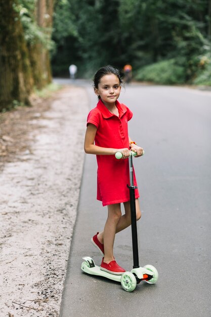 Retrato de una niña de pie sobre scooters en carretera