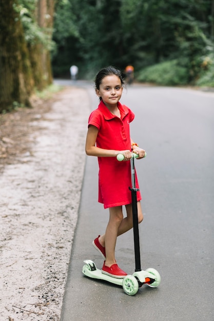 Retrato de una niña de pie sobre scooters en carretera